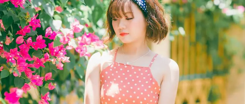 woman in orange polka-dot spaghetti strap dress standing near pink and green plants